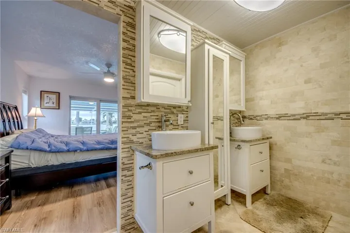 Bathroom with connected bathroom, two vanities, a sink, and tile walls