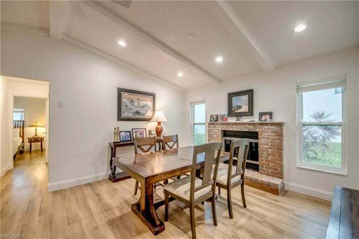 Dining space with light wood-style flooring, a fireplace, lofted ceiling with beams