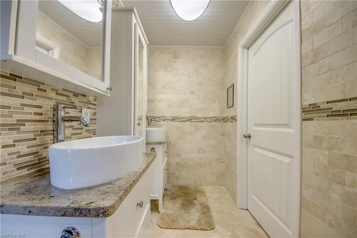 Bathroom with tile patterned floors, tasteful backsplash, tile walls, and vanity