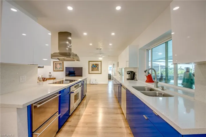 Kitchen with island range hood, modern cabinets, black electric cooktop, white cabinetry, and a sink