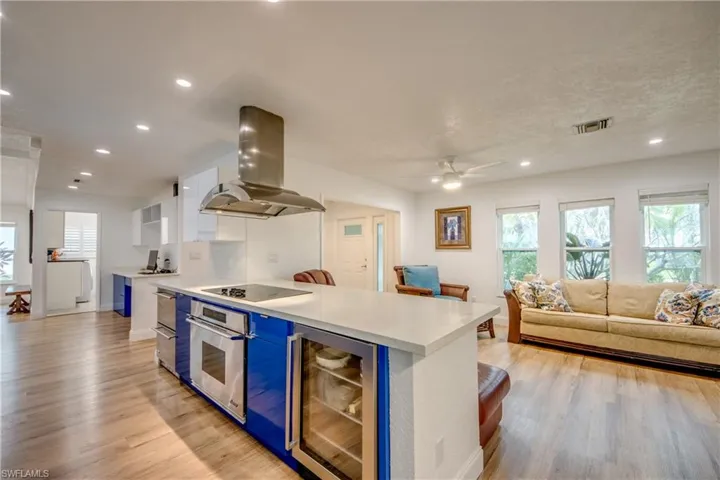 Kitchen with wine cooler, light countertops, stainless steel oven, island range hood, and black electric cooktop