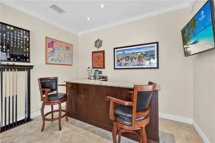 Built-in bar with a granite countertop, recessed lighting, and crown molding
