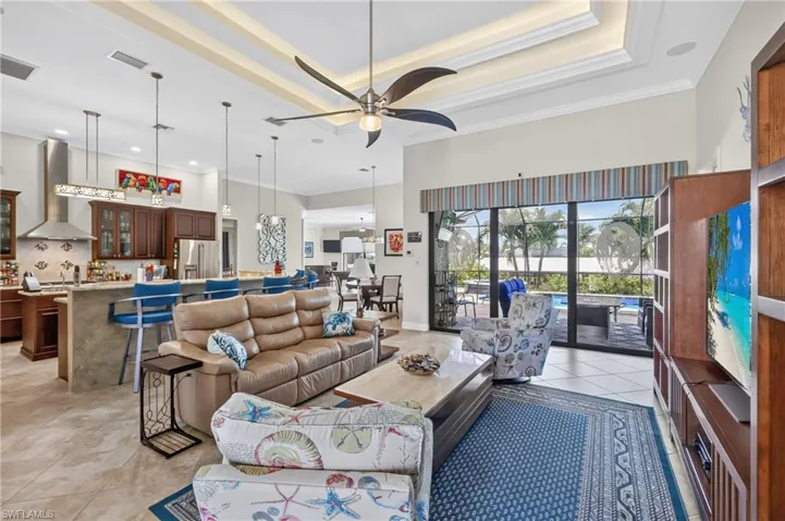 Spacious open-concept living area featuring large format tile flooring, a tray ceiling with recessed lighting and a ceiling fan, and sliding glass doors opening to a lanai with a pool