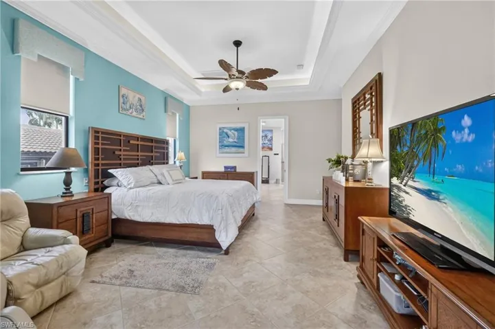 Spacious bedroom featuring neutral tile flooring, a tray ceiling with crown molding, a ceiling fan, and recessed lighting