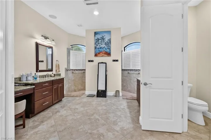 Spacious bathroom featuring twin vanity areas with granite-finish countertops and dark wood cabinetry