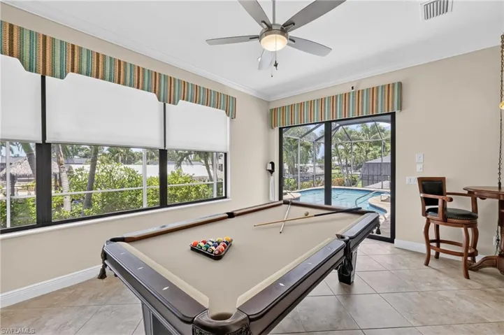 Recreation room with tile flooring and a ceiling fan, featuring a large window with horizontal blinds and a sliding glass door leading to a screened pool area
