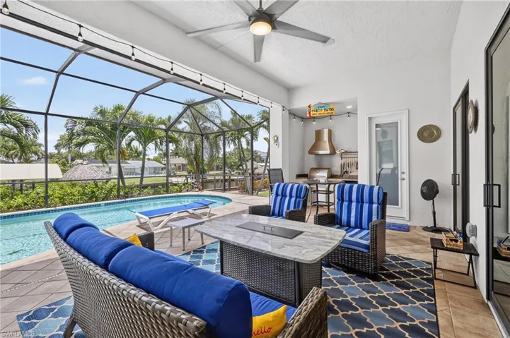 Screened outdoor living area featuring a built-in outdoor kitchen with a stainless steel grill and range hood, a ceiling fan, and string lighting