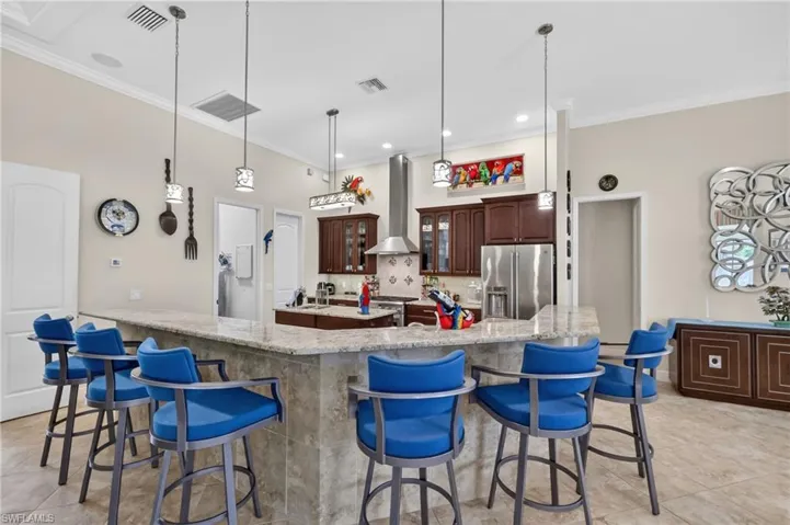 Spacious kitchen featuring a large granite-topped island with seating, stainless steel appliances, dark wood cabinetry, and recessed lighting