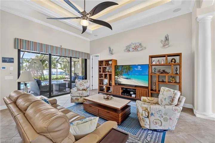 Spacious living area featuring large format tile flooring, a tray ceiling with crown molding and a ceiling fan, and expansive sliding glass doors opening to the screened patio and swimming pool