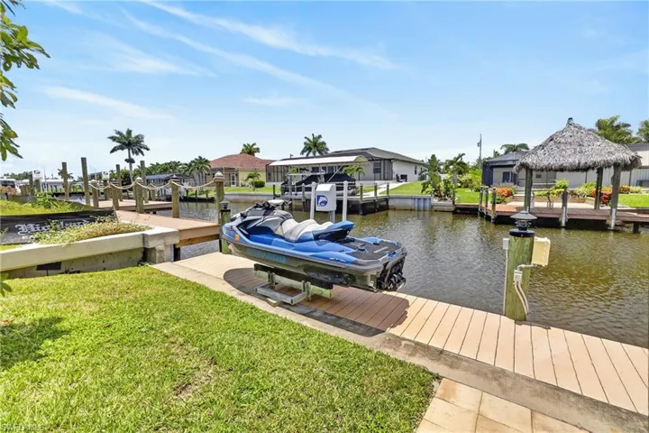 Waterfront property featuring a private boat lift, a wood-finish dock, and lush green lawn