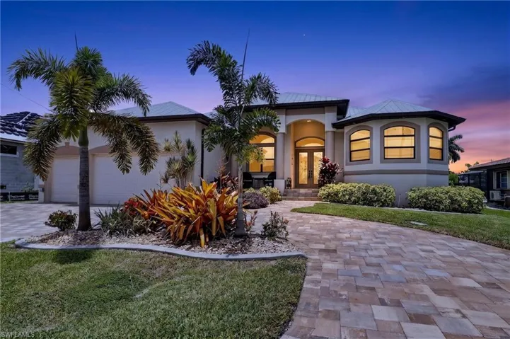 Stucco exterior with a circle paver driveway, arched double entry doors, a multi-pane bay window, and a landscaped front yard with mature palm trees