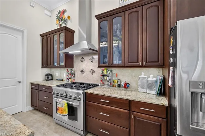 Kitchen featuring a stainless steel range with a coordinating hood, dark wood cabinetry, light-toned countertops, tile flooring, and a tiled backsplash with decorative accents