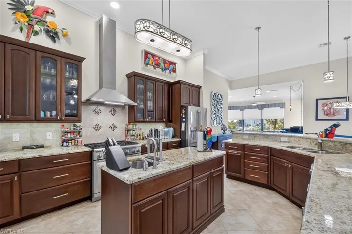 Gourmet kitchen with rich wood cabinetry, granite countertops, stainless steel appliances, a tiled backsplash, and an island with a built-in sink
