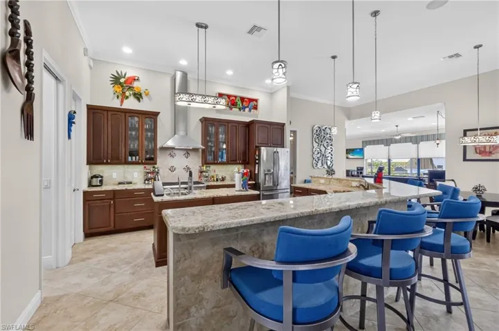 Spacious kitchen featuring an expansive breakfast bar with a stone countertop, wood cabinetry, stainless steel appliances, and recessed lighting