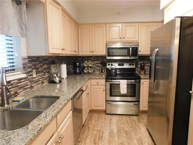 Kitchen with light brown cabinets, sink, light hardwood / wood-style flooring, appliances with stainless steel finishes, and light stone counters