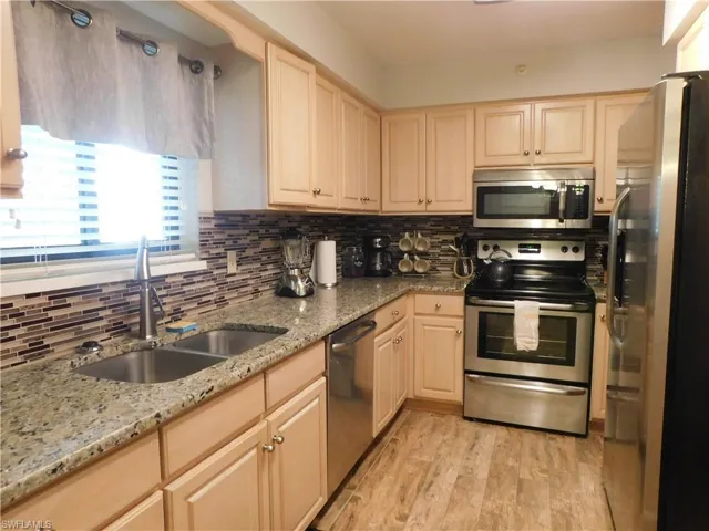 Kitchen with light stone countertops, light wood-type flooring, stainless steel appliances, sink, and light brown cabinets