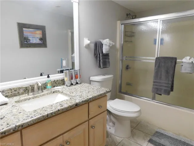 Full bathroom featuring shower / bath combination with glass door, tile patterned floors, vanity, and toilet