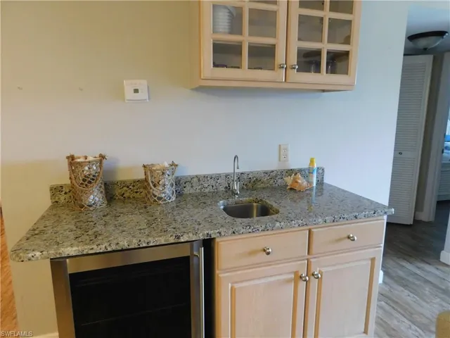 Kitchen with light stone countertops, sink, light brown cabinets, wine cooler, and light hardwood / wood-style flooring