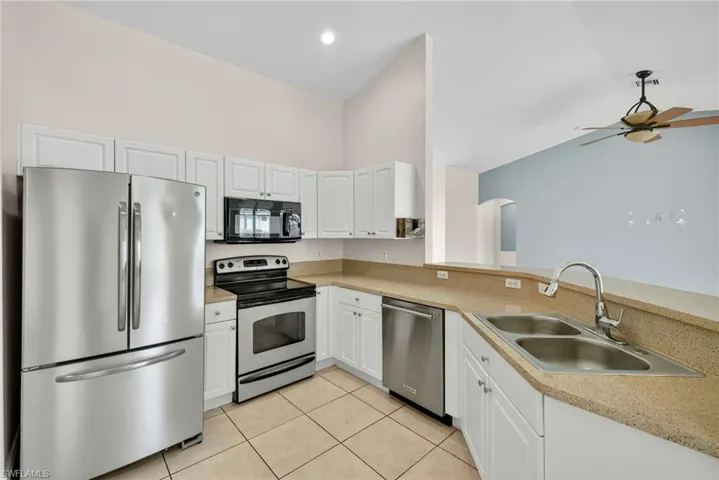 Kitchen with stainless steel appliances, light tile patterned flooring, light countertops, white cabinets, and ceiling fan