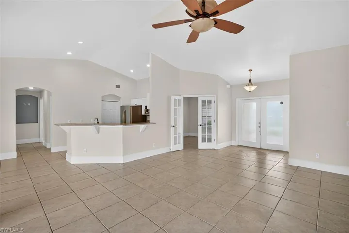 Unfurnished living room featuring french doors, light tile patterned floors, arched walkways, lofted ceiling, and ceiling fan