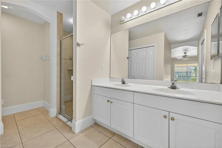 Full bath with light tile patterned floors, a shower stall, double vanity, and a ceiling fan