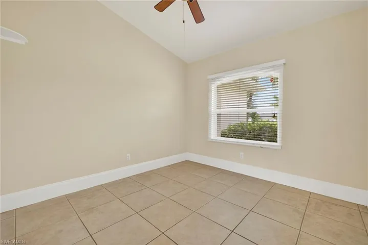 Empty room with vaulted ceiling, light tile patterned floors, and a ceiling fan