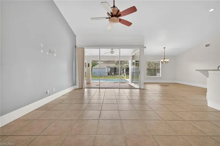 Empty room featuring light tile patterned floors, lofted ceiling, a sunroom, ceiling fan, and a chandelier