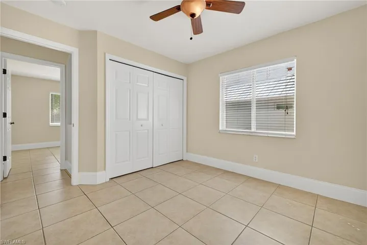 Unfurnished bedroom featuring light tile patterned floors, ceiling fan, multiple windows, and a closet