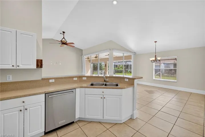 Kitchen featuring white cabinets, dishwasher, a peninsula, light stone counters, and vaulted ceiling