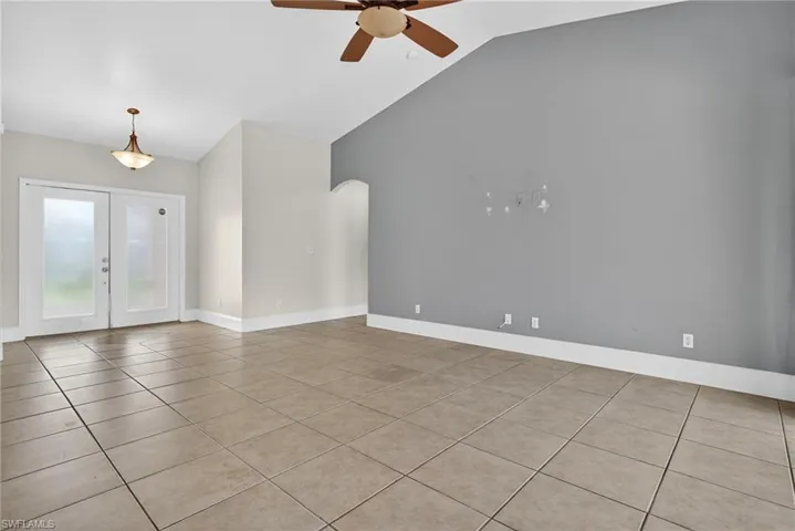 Empty room featuring light tile patterned flooring, french doors, a ceiling fan, lofted ceiling, and arched walkways