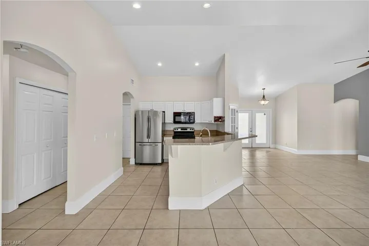 Kitchen with arched walkways, a kitchen breakfast bar, freestanding refrigerator, french doors, and light tile patterned floors
