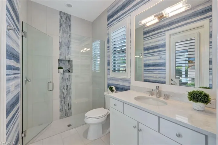 Bathroom with toilet, a shower with shower door, a healthy amount of sunlight, and vanity