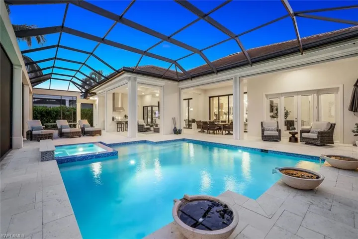 View of pool with an in ground hot tub, an outdoor living space with a fire pit, a patio area, and glass enclosure
