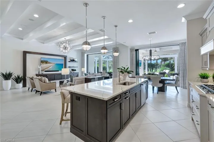 Kitchen featuring a center island with sink, hanging light fixtures, light stone counters, white cabinetry, and sink