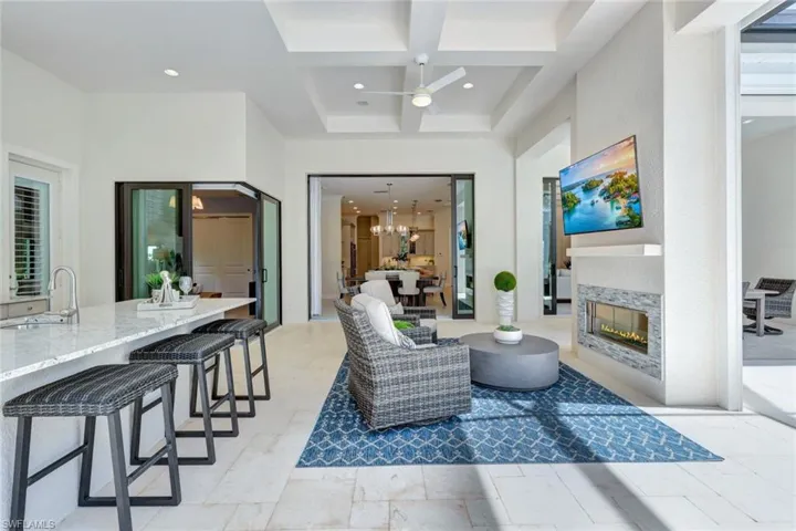 Living room with beam ceiling, coffered ceiling, sink, and ceiling fan with notable chandelier
