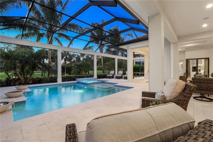 Pool at dusk featuring an in ground hot tub, a patio, and glass enclosure