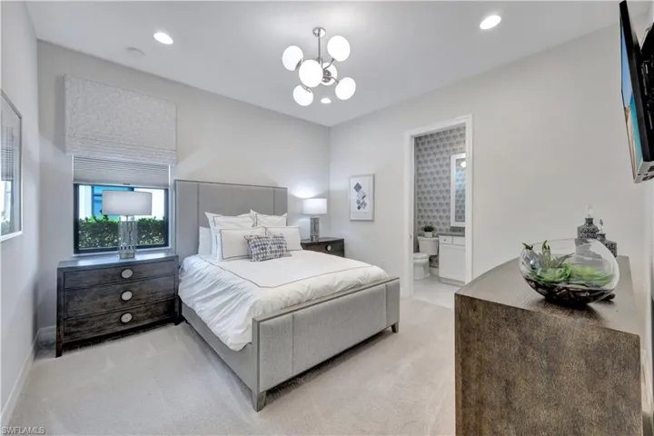 Carpeted bedroom featuring ensuite bath and an inviting chandelier