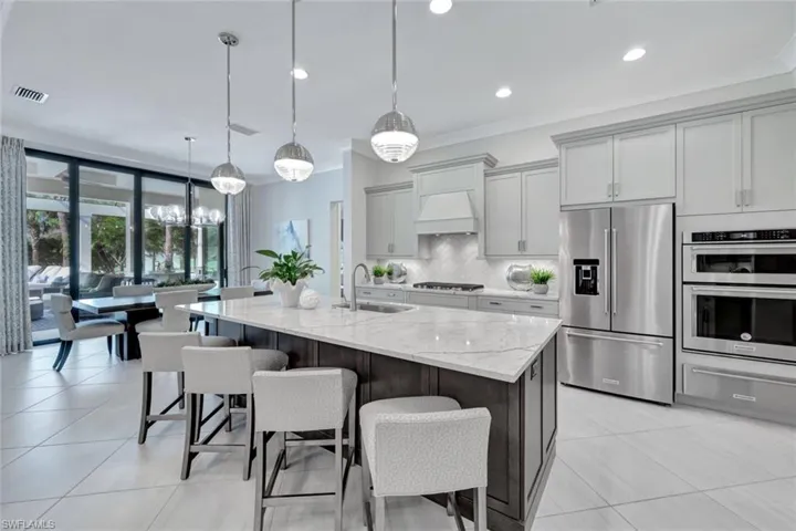 Kitchen with hanging light fixtures, light stone counters, an island with sink, sink, and stainless steel appliances