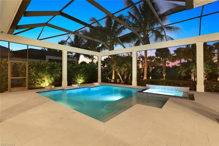 Pool at dusk featuring an in ground hot tub, a patio area, and glass enclosure