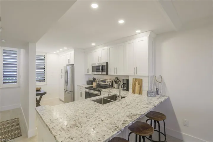Kitchen featuring a breakfast bar area, stainless steel appliances, light stone countertops, a peninsula, and white cabinetry