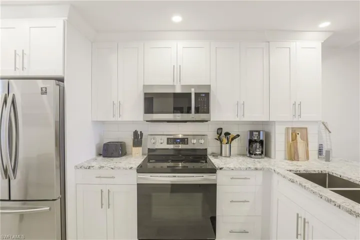 Kitchen featuring stainless steel appliances, light stone countertops, white cabinetry, backsplash, and recessed lighting