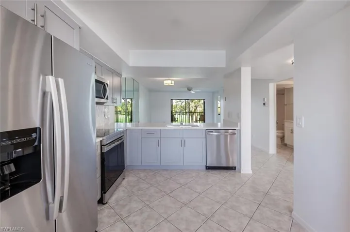 Kitchen with a tray ceiling, light countertops, light tile patterned floors, stainless steel appliances, and ceiling fan