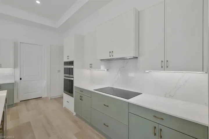 Kitchen with black electric cooktop, light wood-type flooring, decorative backsplash, stainless steel double oven, and dual tone cabinetry