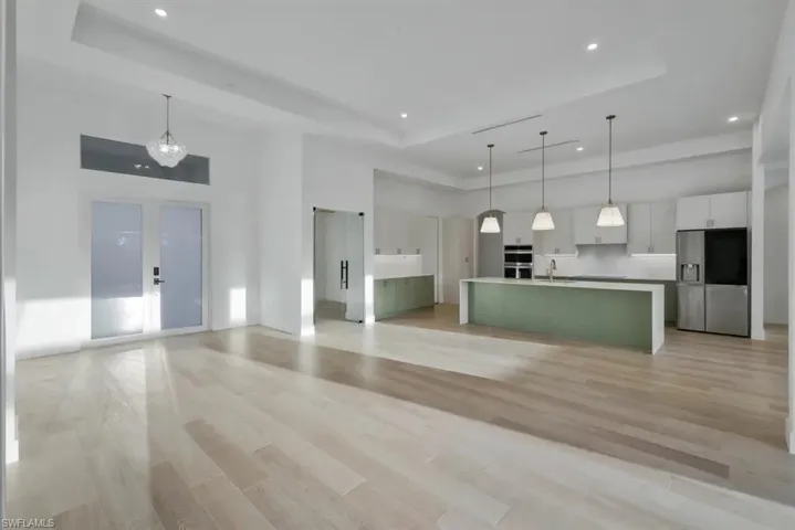 Unfurnished living room with a high tray ceiling, light wood-type flooring, recessed lighting, and french doors