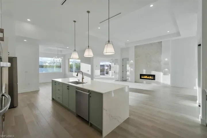 Kitchen featuring green cabinetry, a kitchen island with sink, a glass covered fireplace, open floor plan, and light wood-type flooring