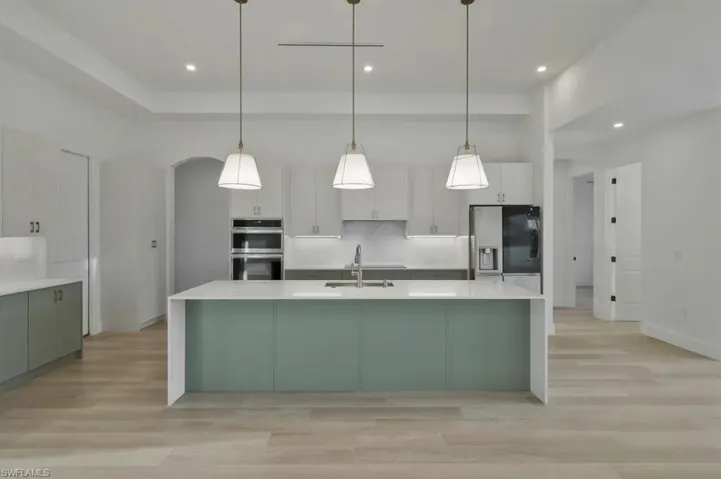 Kitchen with light wood-style flooring, light stone countertops, two tone cabinetry, stainless steel appliances, and hanging light fixtures