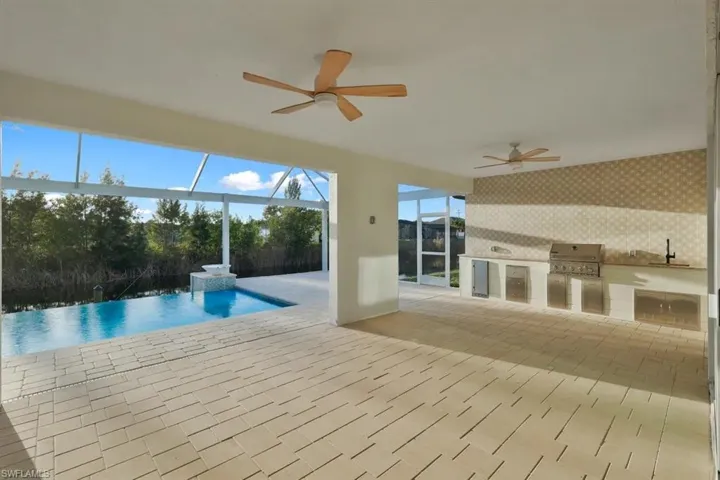 View of pool with exterior kitchen, patio surround, glass enclosure, an infinity pool, and a sunroom