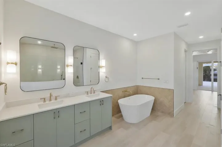 Full bath featuring a soaking tub, double vanity, light wood-style flooring, a wainscoted wall, and recessed lighting
