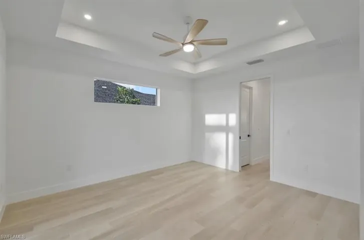 Unfurnished room with light wood-type flooring, a ceiling fan, a raised ceiling, and recessed lighting