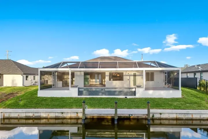 Back of property featuring a sunroom, a lawn, an outdoor pool, and glass enclosure